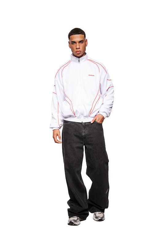 Man wears Rave Trackjacket White Red with red piping, zipper, stand-up collar, OLAKALA logo and elastic cuffs, with wide black jeans and grey sneakers.