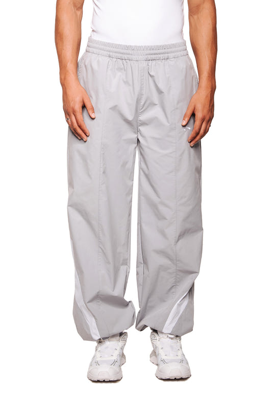 Person trägt die Sports Trackpants Gray aus robustem Rip-Stop-Gewebe mit elastischem Bund; zeigt gesticktes OLAKALA Sports Logo am linken Bein.
