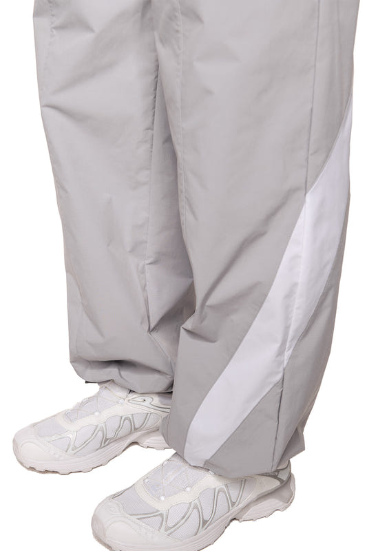 Nahaufnahme der Sports Trackpants Gray mit weißem Seitenstreifen, elastischem Bund und gesticktem OLAKALA Sports Logo auf dem linken Hosenbein, getragen mit weißen Sneakers.