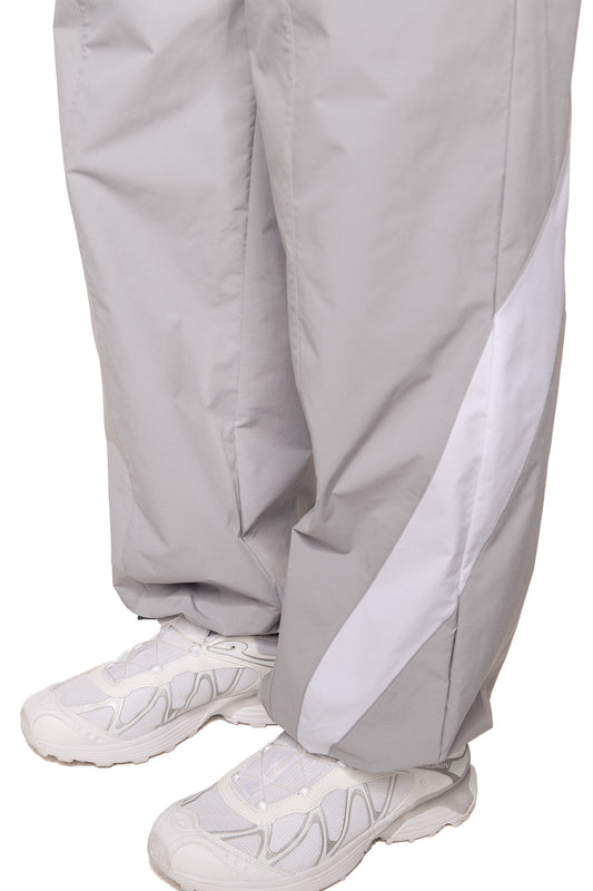 Nahaufnahme der Sports Trackpants Gray mit weißem Seitenstreifen, elastischem Bund und gesticktem OLAKALA Sports Logo auf dem linken Hosenbein, getragen mit weißen Sneakers.