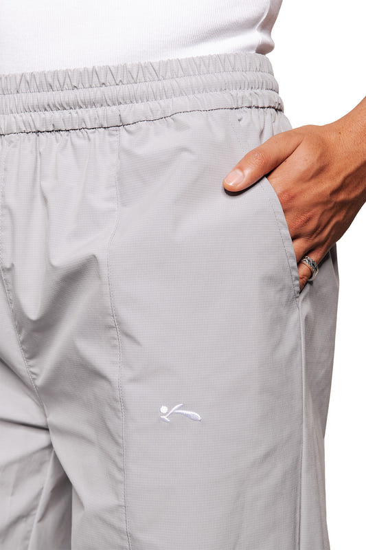 Person trägt graue Sports Trackpants mit elastischem Bund, Hand in der Seitentasche. Gesticktes OLAKALA Sports Logo unter der Tasche sichtbar.