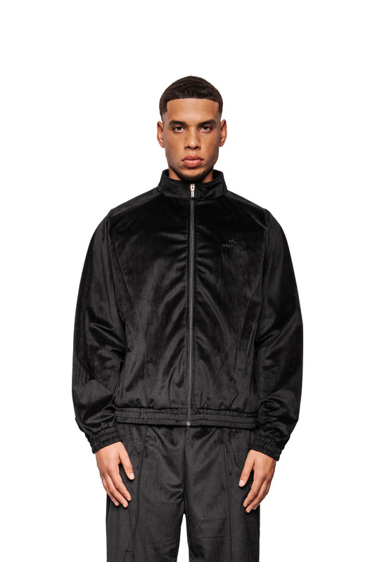 Männliches Model trägt die Sports Velour Jacket Black mit hohem Kragen, Reißverschluss, elastischen Abschlüssen und gesticktem Logo, präsentiert sportlich-modernen Look.