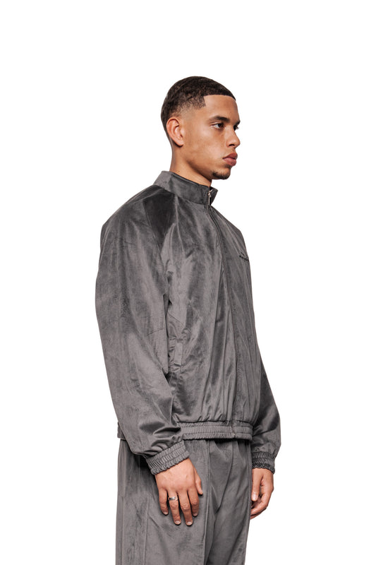 Junger Mann im Profil trägt Sports Velour Jacket Gray, zip-up mit Teilungsnähten, elastische Bündchen, lockeren Hosen; betont sportlich-modernen Look und hohen Tragekomfort.