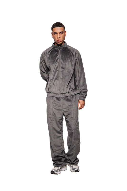 Modell trägt Sports Velour Jacket Gray: Velours-Jacke mit Stehkragen, Teilungsnähten, Mesh-Futter, elastischen Bündchen und lockerer Passform, kombiniert mit passenden Jogginghosen.