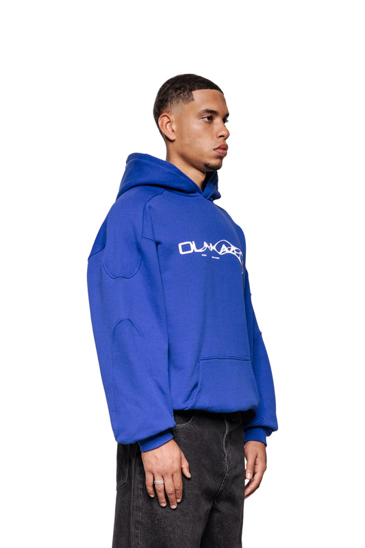 Männliches Model trägt Synergy Mask Hoodie Blue mit Siebdruck-Grafik auf der Brust, Ripp-Bündchen und Kängurutasche, kombiniert mit dunklen Jeans.