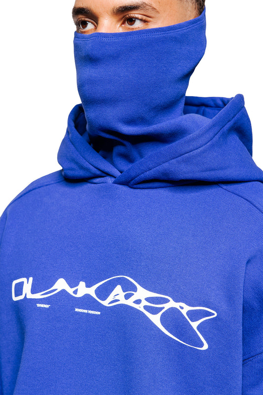 Person wears the Synergy Mask Hoodie Blue with integrated face protection and Synergy graphics on the chest. Oversized fit and ribbed details on the sleeves and hem.
