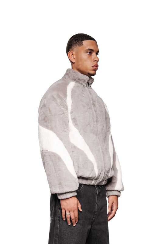 Junger Mann in profilansicht trägt eine graue Two-Toned Fur Jacket mit weißen Streifen, Reißverschluss und Eingriffstaschen. Lockerer Schnitt, unisex Design.