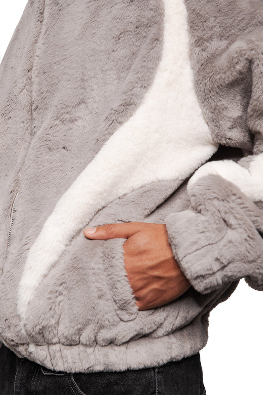 Close-up of a gray two-toned fur jacket with white inserts, stand-up collar, raglan sleeves and elastic waistband, worn casually with one hand in the side pocket.