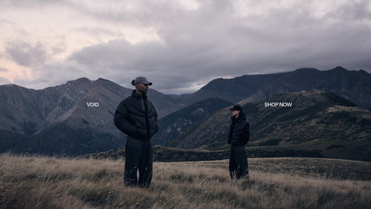 Zwei Personen in dunklen Daunenjacken stehen auf einer grasigen Bergwiese vor einer Gebirgskette mit wolkigem Himmel; Textüberlagerungen 