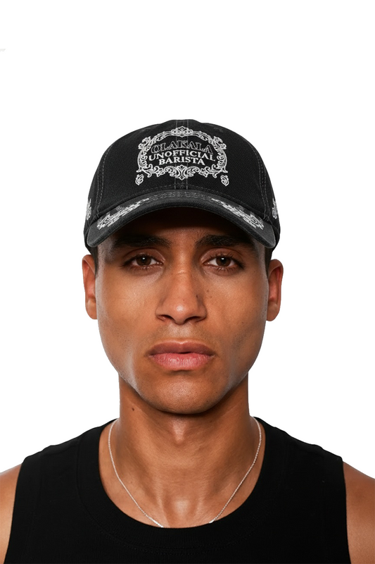 Person trägt die Mokka Cap mit UNOFFICIAL BARISTA-Stickerei und verstellbarem Verschluss, kombiniert mit einem schwarzen Tanktop und silberner Halskette.