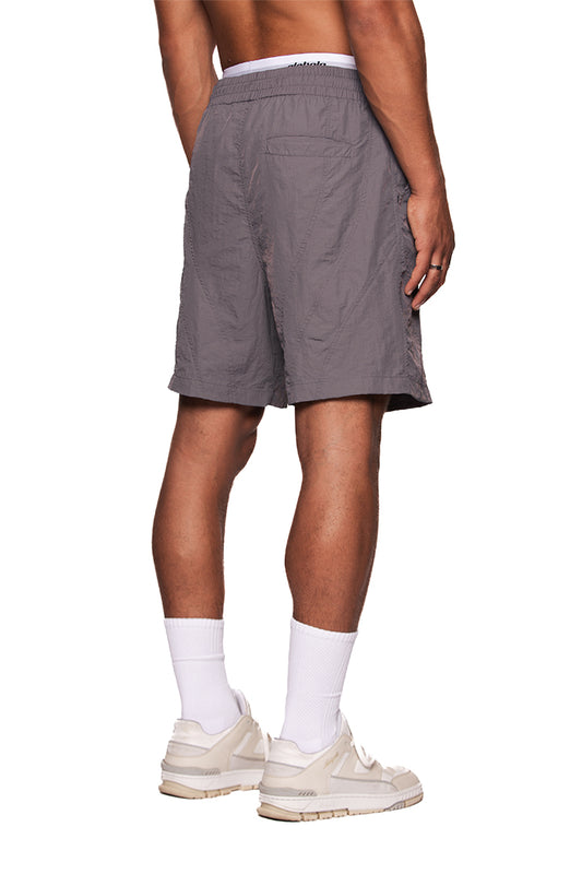 Person trägt Naxos Swim Shorts Gray mit französischen Taschen, verstellbarem Bund und reflektierendem OLAKALA-Logo auf dem linken Bein.