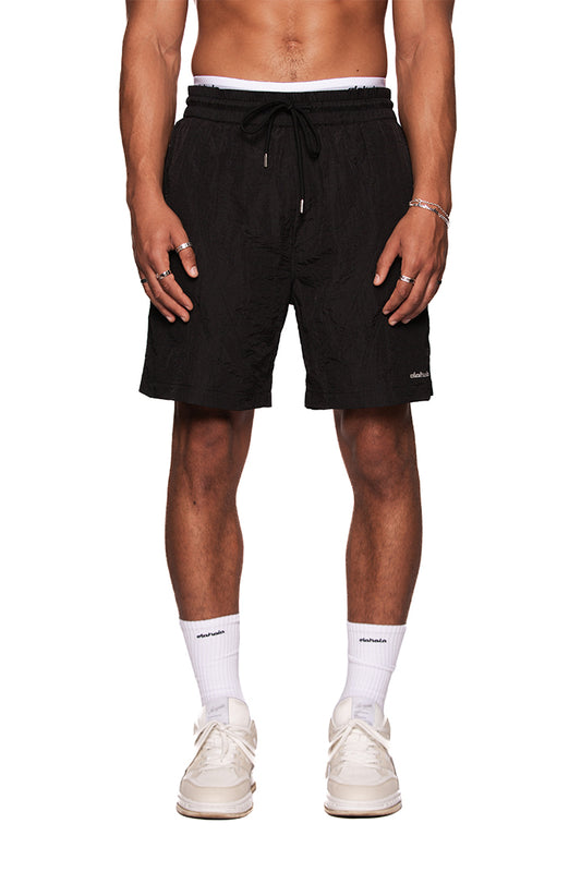 Mann trägt Naxos Swim Shorts Black mit verstellbarem Bund und reflektierendem OLAKALA-Logo auf dem linken Bein.