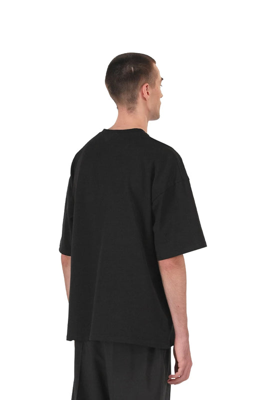 Man in black CC T-shirt with embroidered OLA KALA logo on the chest, oversized fit, part of the Core Collection by OLAKALA.