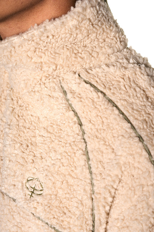Distorted Teddy Jacket mit gesticktem OLAKALA-Logo, Paspelierungen, elastischen Bündchen und Eingriffstaschen, aus warmem Fleece-Stoff, zeigt eine nahaufnahme der Textur.