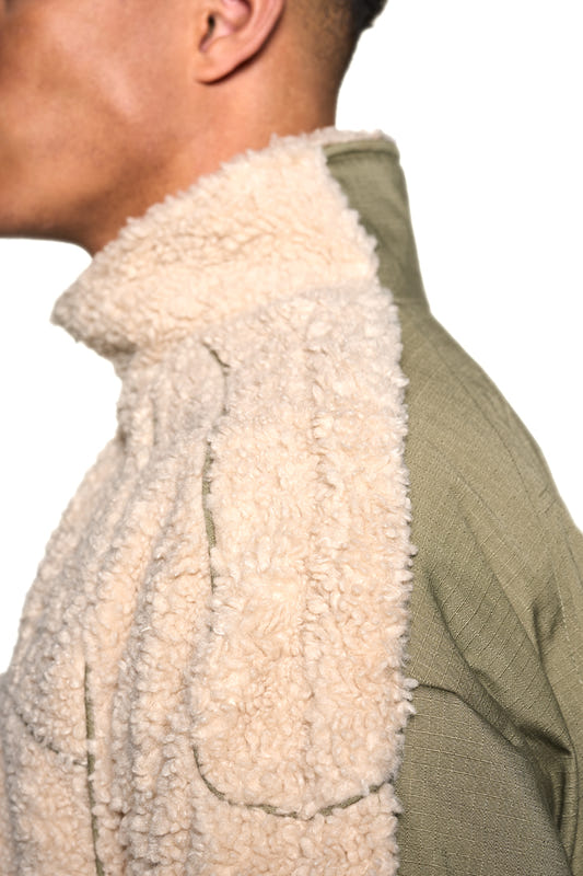 Nahaufnahme der Distorted Teddy Jacket mit Paspelierung, elastischen Bündchen, eingesticktem OLAKALA-Logo und Defect Identity-Icon; oversized und unisex, aus warmem Fleece-Stoff.